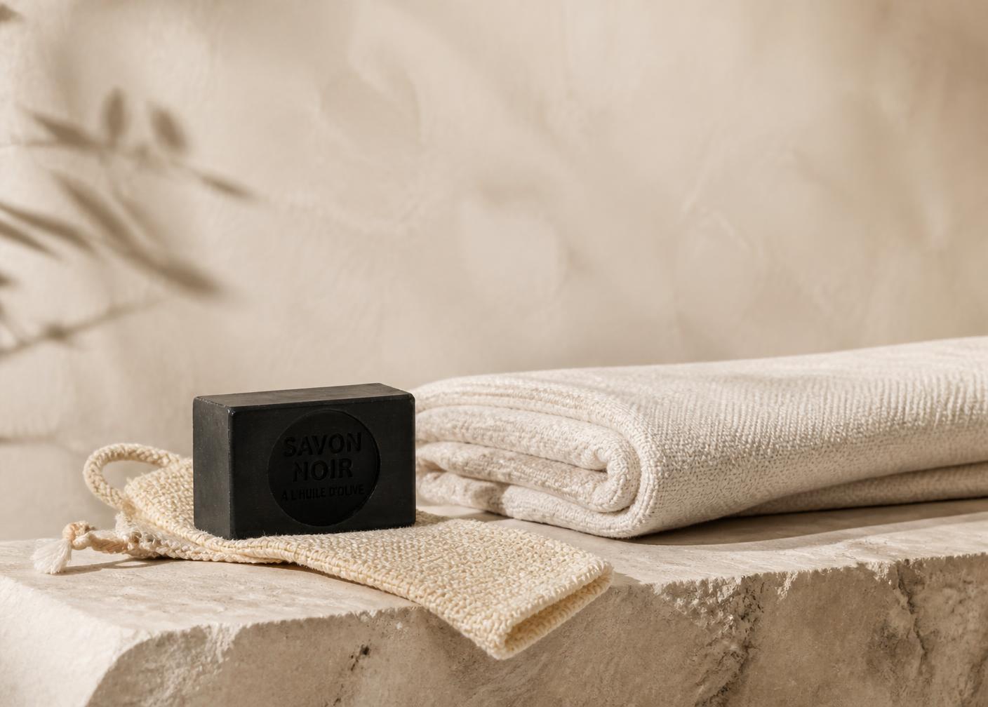 Savon noir, gant kessa et linge écru posés sur de la pierre naturelle